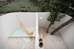 A minimalist outdoor patio featuring concrete walls, sand flooring, and a natural fiber hammock.