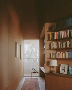 A cozy modern home library featuring tall shelves filled with books, a stylish chair, and a window providing natural light.