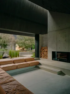 Modern industrial living room with concrete walls and floor, featuring a leather sofa and a concrete fireplace.