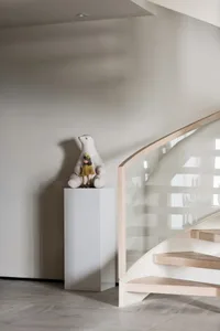 A modern staircase features glass railings and a wooden step, accompanied by a decorative glass sculpture of a bear holding a
