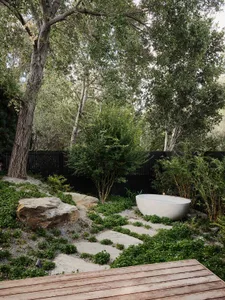 A tranquil outdoor spa area featuring a natural stone tub, surrounded by gravel pathways and lush greenery.
