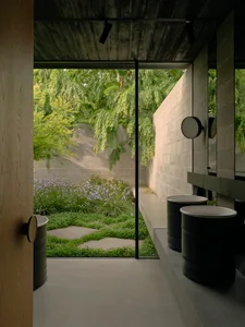 Modern gray bathroom interior with concrete materials and an outdoor view of greenery.