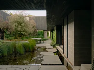A modern house with a concrete exterior features a garden with water features, pathways, and greenery.