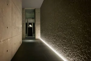 A modern interior space featuring textured concrete walls with lighting along the bottom edge, creating a minimalist and slee