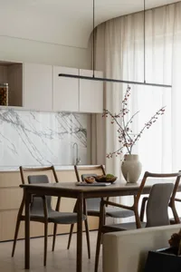 Modern residential kitchen featuring a wooden dining table, marble backsplash, and textile upholstery chairs.