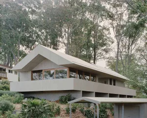 Modern concrete and metal house exterior with large windows and greenery surrounding.