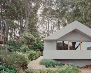 A modern minimalist house with a concrete exterior surrounded by lush greenery and a pathway.