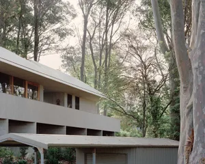 Moderate residential structure composed of concrete materials surrounded by lush greenery and tall trees.