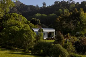 Minimalist residential cabin with corrugated metal exterior, surrounded by lush greenery and trees