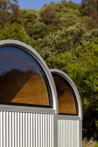 A modern architectural structure made of corrugated metal with curved windows and wooden interiors.