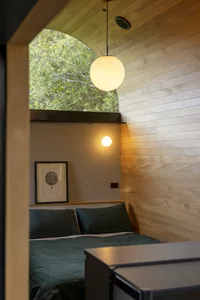A minimalist bedroom featuring wooden walls and a green bedspread.