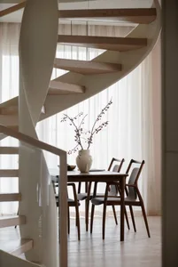 A modern minimalist dining room featuring a wooden table, chairs, and a vase with branches.