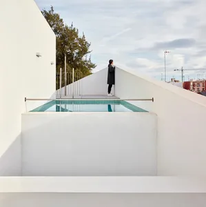 Person standing on minimalist concrete pool deck, overlooking cityscape.