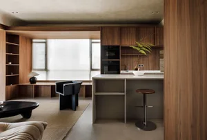A modern residential kitchen featuring walnut furniture, black stools, and a minimalist design.