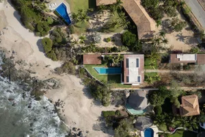 Aerial view of beachfront homes featuring a modern design with concrete, clay, and glass materials, surrounded by tropical pa
