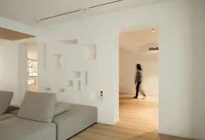 A minimalist living room with a sofa and a woman walking in the background.