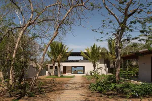 Modern exterior of a concrete home with a clear blue sky and surrounded by trees.