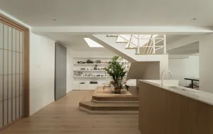 Modern interior design featuring a living room with a kitchen area and a staircase, using wood and white materials.