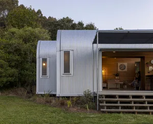 A contemporary metal-clad residential extension with a corrugated roof, large windows, and a serene outdoor setting.