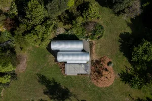 Aerial view of a minimalist house with a corrugated metal roof surrounded by greenery.