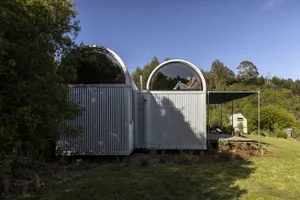 A small, minimalist cabin constructed from metal with rounded windows and a covered porch.