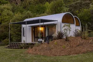 A metal studio hut with a curved roof nestled in a forested area.