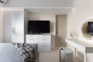 A modern bedroom with white furniture and a television on a cabinet.