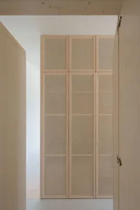 A tall, wooden closet with cane mesh doors and a light, open design.
