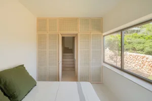 Minimalist bedroom featuring wooden furniture and a large window overlooking greenery.