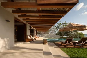 Modern minimalist residential patio with wooden furniture, thatched umbrella, and infinity pool.