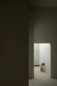 Minimalist modern interior with concrete walls and floor, featuring a simple chair leaning against a wall.