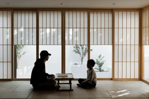 Two people in silhouette sitting in a room with wooden sliding doors and a plant in the background.