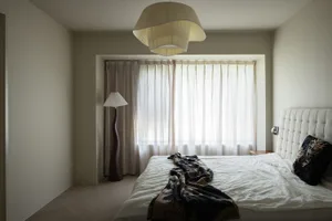 A minimalist bedroom with light-colored walls, a bed with a tufted headboard, and curtains.