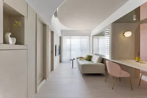 A minimalist living room with concrete walls, a white sofa, and a pink chair.