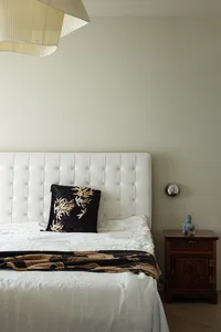 A modern bedroom featuring a black and white bed with a quilted headboard and a dark wooden bedside table with a Buddha statu