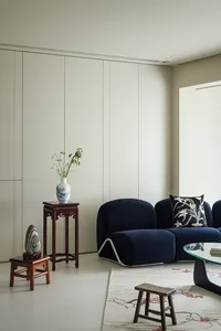 A modern living room featuring a blue fabric couch with a white pillow, a white vase with flowers on a wooden pedestal, and a