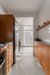 A minimalist kitchen features wooden cabinets with white countertops and floor tiles.