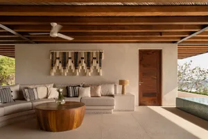 Modern minimalist living room featuring concrete surfaces, a round wooden coffee table, and a woven tapestry wall hanging.