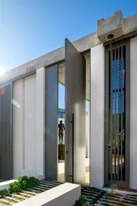 Modern exterior architectural design featuring a concrete and glass entryway bordered by a botanical garden.