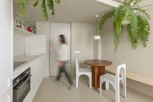 A modern kitchen with white minimalist design, featuring a wooden table, white chairs, and glass materials.