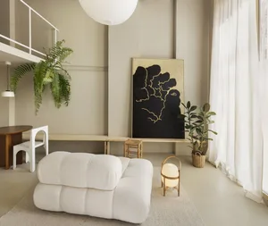 A modern living room with neutral tones, featuring plush seating, artistic wall decor, and indoor plants.