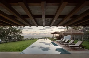 A modern poolside lounge area featuring wooden structures and thatched roofing.