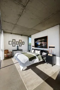 A modern industrial bedroom with concrete walls, a bed, and various framed pictures on the wall.