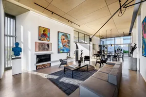 Modern minimalist living room with concrete walls and floor, featuring a large sofa, coffee table, fireplace, and abstract ar