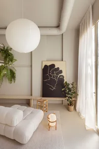 Modern minimalist living room with white walls, a white sofa, and a light fixture suspended from the ceiling.