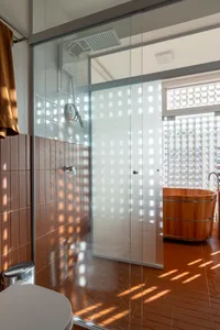 A modern bathroom featuring white and brown ceramic tiles, a glass shower enclosure, and a wooden bathtub.