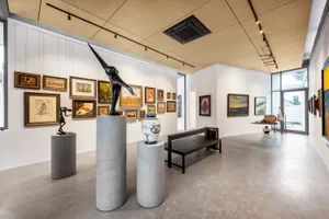 Modern art gallery with concrete pillars, wooden benches, and various paintings and sculptures on the walls.