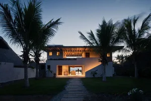 A modern residential house with a concrete exterior and glass windows, viewed from the garden at dusk.