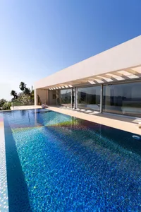 A modern house featuring a glass wrap-around pool under a clear blue sky.