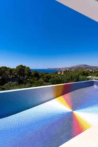 A modern landscape featuring colorful mosaic tiles in the foreground, with a view of a blue sky, sea, and greenery in the dis